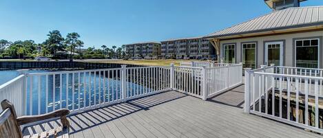 A wooden deck with a pool, white railings, and a view of a multi-story building in the background.