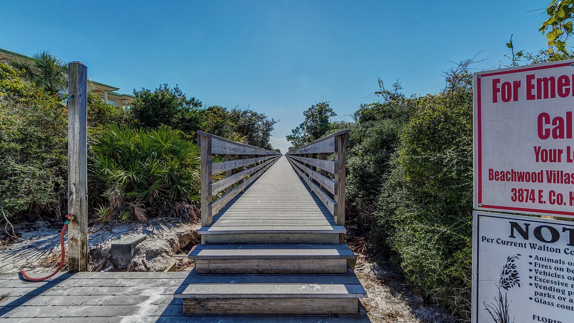 Une promenade en bois mène aux villas de Beachwood, et un panneau indique les coordonnées des personnes à contacter en cas d’urgence.