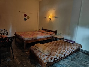 A room with two beds, a chair, a small table, and a wall-mounted light fixture. - Yatri Villa in Mulshi (Paud)