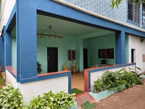 A building with a blue exterior, a covered porch, and a door leading to an interior space.