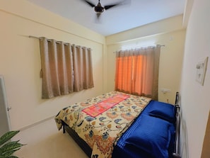 A bedroom with a bed, curtains, a ceiling fan, and a window. - Yatri Villa in Mulshi (Paud)