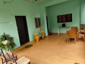 A room with a wooden floor, a black door, a window, a wall-mounted artwork, and wicker furniture.