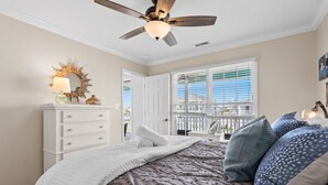 A bedroom with a bed, a ceiling fan, a dresser, a window with blinds, and a view of the outside. - 4 Bedroom 3 Bath walking distance to everything + hot tub! (Holden Beach)