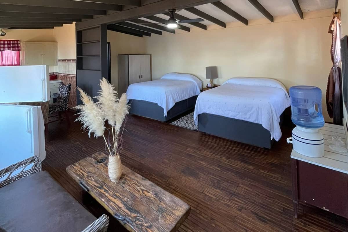 A room with two beds, a small table with a vase, a water dispenser, and a refrigerator.