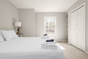 Ein Schlafzimmer mit Bett, Nachttisch mit Lampe, Fenster und Kleiderschrank.