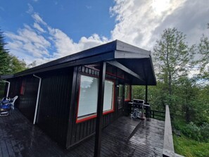 Une cabane moderne dotée d’une terrasse en bois, de grandes fenêtres et d’un espace extérieur couvert.