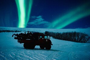 Un paysage enneigé avec un véhicule et des aurores boréales.