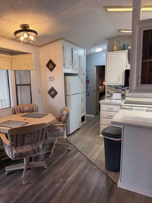 A compact kitchen with white cabinets, a refrigerator, a toaster, and a dining area with a table and chairs.