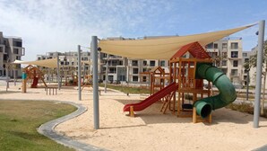 A playground with slides and climbing structures, surrounded by a sandy area and a paved walkway. - Spacious 3-bedroom apartment in tranquil Cairo with AC (Cairo Governorate)