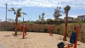 An outdoor exercise area with fitness equipment, palm trees, and a stone wall. - Spacious 3-bedroom apartment in tranquil Cairo with AC (Cairo Governorate)
