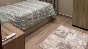 A bedroom with a bed, a wooden wardrobe, a bedside table with a remote control, and a patterned rug. - Spacious 3-bedroom apartment in tranquil Cairo with AC (Cairo Governorate)
