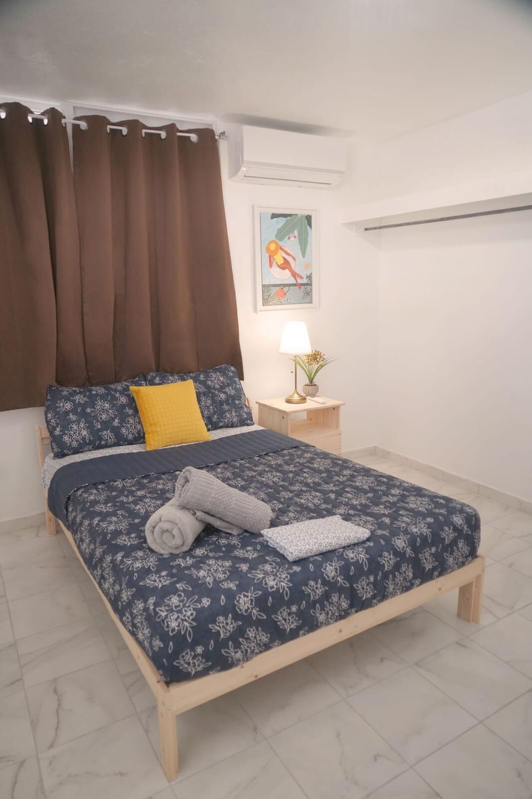 Uma cama bem arrumada com roupa de cama floral, um abajur e uma mesinha de cabeceira com uma planta.