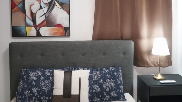 Une chambre à coucher avec un lit, une table de chevet, une lampe, un tableau et un rideau marron.