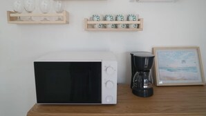 Une cuisine équipée d’un four à micro-ondes, d’une machine à café et d’étagères où sont rangés de la vaisselle et des tasses.