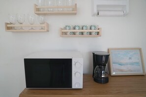 Eine Küche mit Mikrowelle, Kaffeemaschine und Regalen mit Gläsern und Tassen.