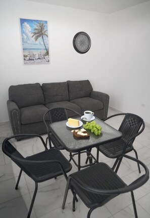 A living area with a gray sofa, a small table with a cup, a plate with food, and a chair. - Apt para 2 / WiFi + Parking / 10 min aeropuerto (Carolina)