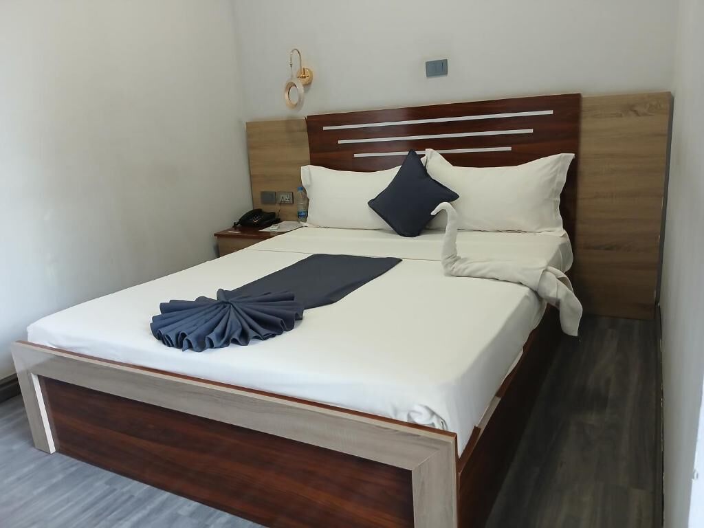 A neatly made bed with a wooden headboard, white bedding, and a dark blue decorative pillow.