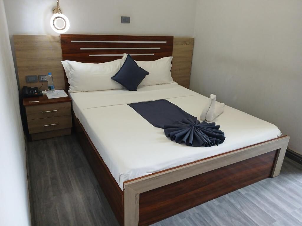 Un lit bien fait, avec une tête de lit en bois, une table de chevet avec une lampe et un luminaire fixé au mur.