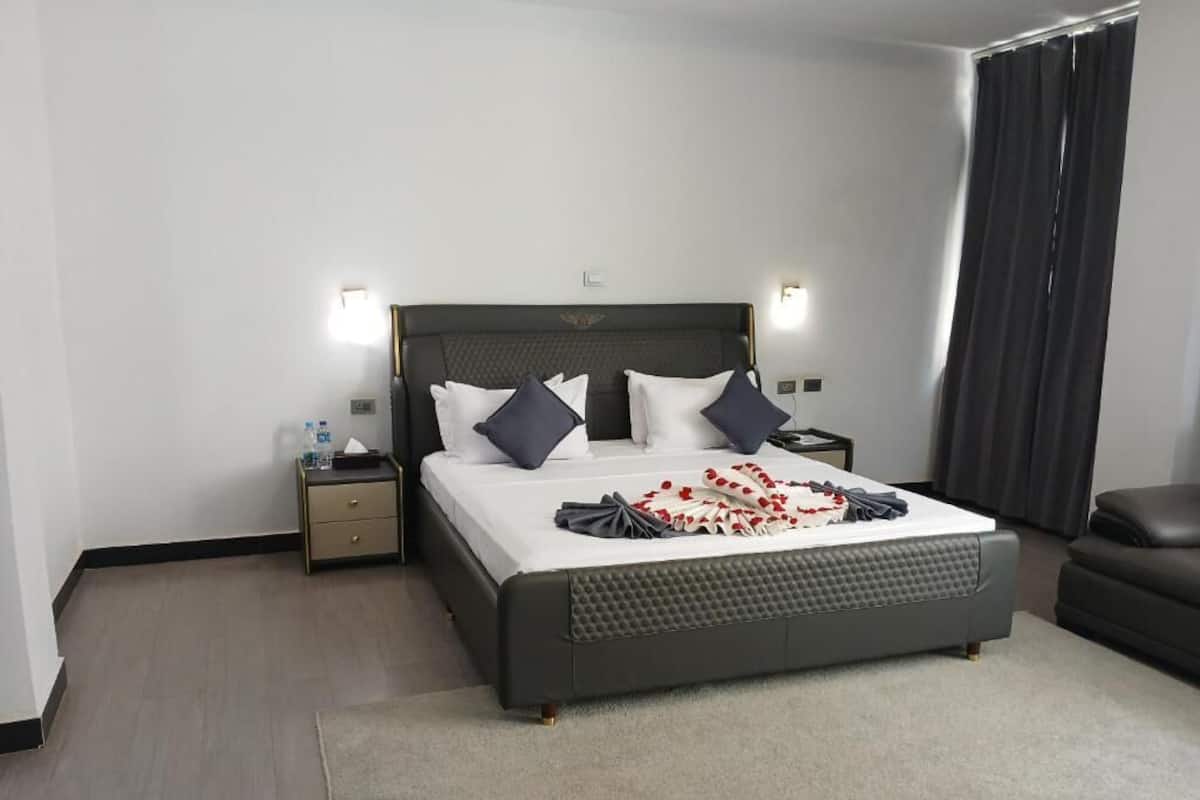 Et moderne hotelværelse med en stor seng, to sengeborde, en mørk sofa og et vindue med gardiner.
