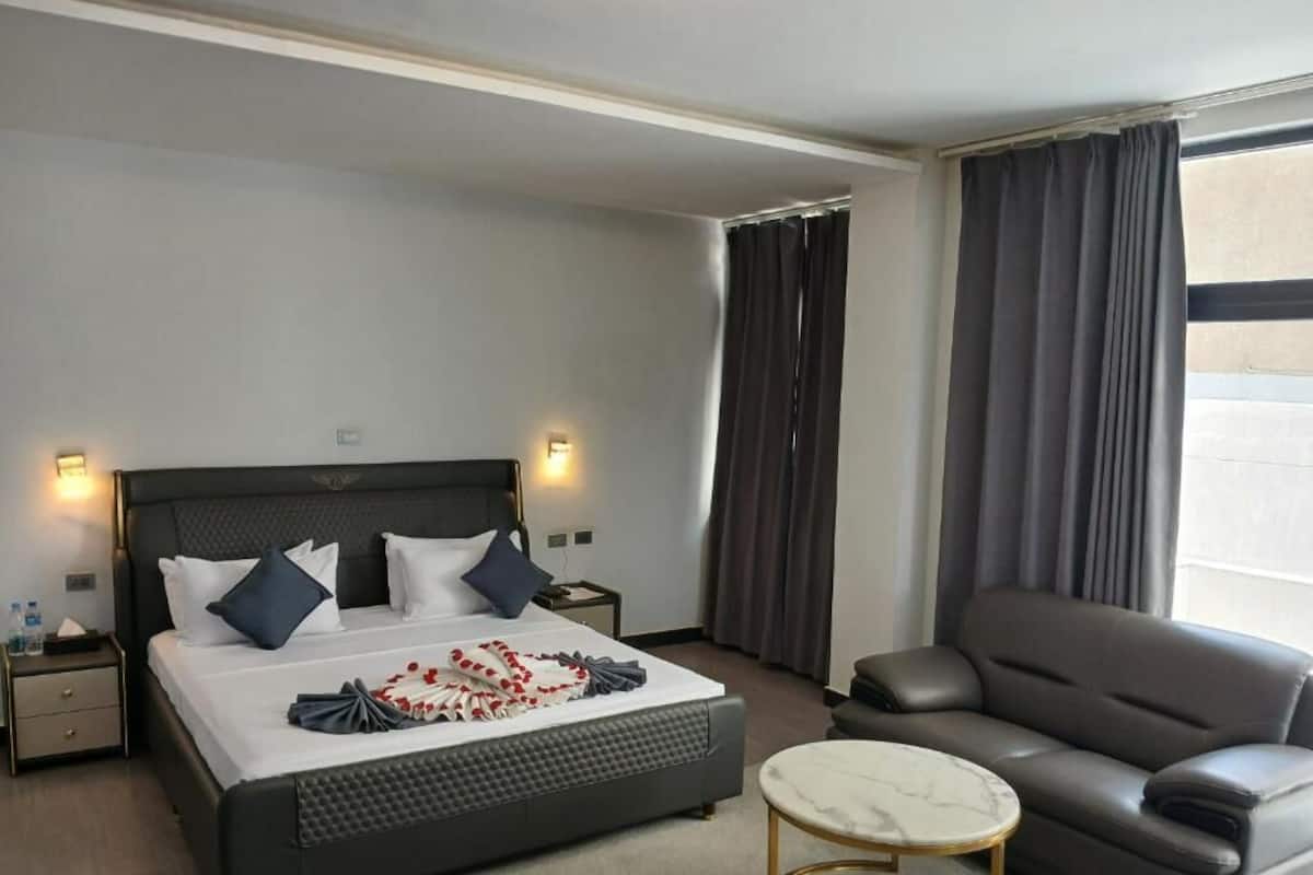 Et moderne hotelværelse med en stor seng, en sofa, et rundt bord og et vindue med gardiner.