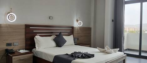 Una camera d'albergo moderna con un letto di legno, comodini, un telefono e vista sulla città attraverso ampie finestre.