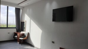 Una habitación de hotel moderna con un ventanal grande, un televisor de pantalla plana en la pared, un banco de madera y un escritorio con una silla.