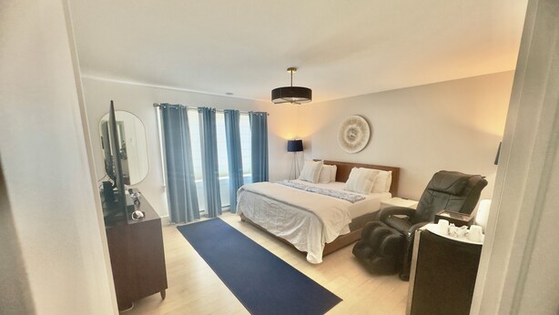 Een hotelkamer met een bed, een massagestoel, een bureau met lamp en uitzicht door het raam.