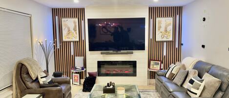 A living room with leather sofas, a glass coffee table, a fireplace, and a flat-screen TV.
