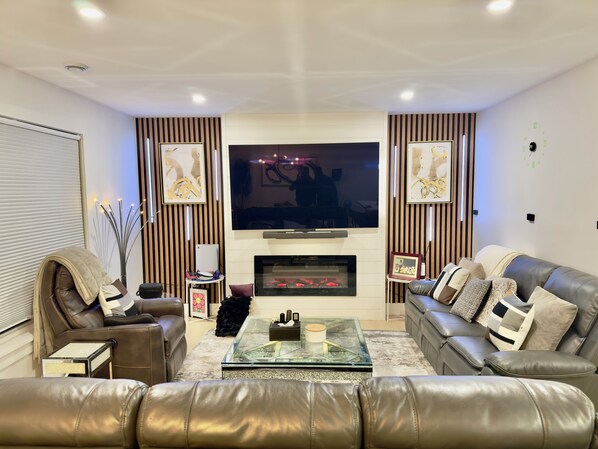 Ein Wohnzimmer mit Ledersofas, einem Glastisch, einem Kamin und einem Flachbildfernseher.