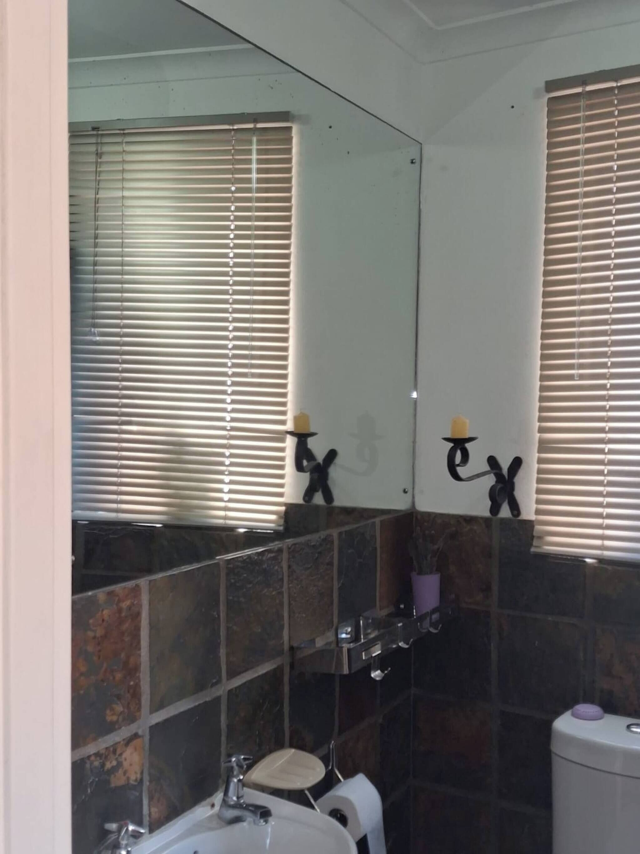 A bathroom with a mirror, two towel racks, a sink, a toilet, and a window with blinds.