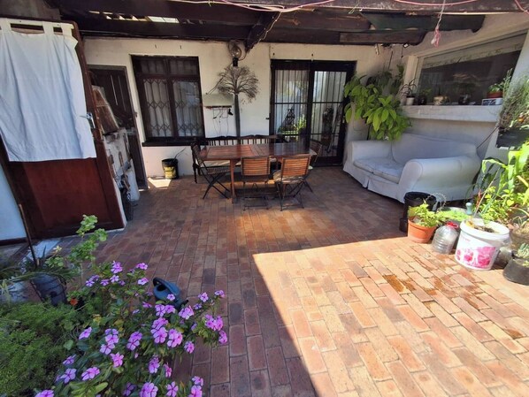 A patio with a wooden table and chairs, a white sofa, and various potted plants.