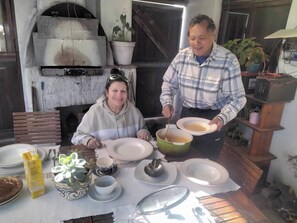Een eetgedeelte met een tafel voor twee personen, een pizzaoven en potplanten.