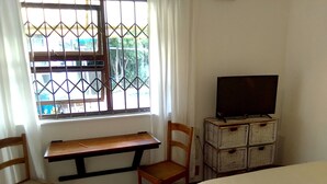 A room with a wooden desk, two wooden chairs, a television on a stand, and a bed. - Adventure Cape Town 1 (Cape Town)
