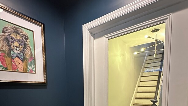 A hallway with a dark blue wall, a white door with a mirror, a staircase with a light fixture, and a framed picture on the wall. - Exc Location & Comfortable Apt 2BD 1BA Downtown JC 12 min to NYC (Jersey City)