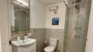 Casa de banho com cabine de chuveiro em vidro, lavatório branco e sanita.
