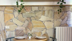 Paredes de pedra com um relógio e um aviso que diz 'Relax' sobre uma mesa posta com pratos, copos e um vaso de planta.