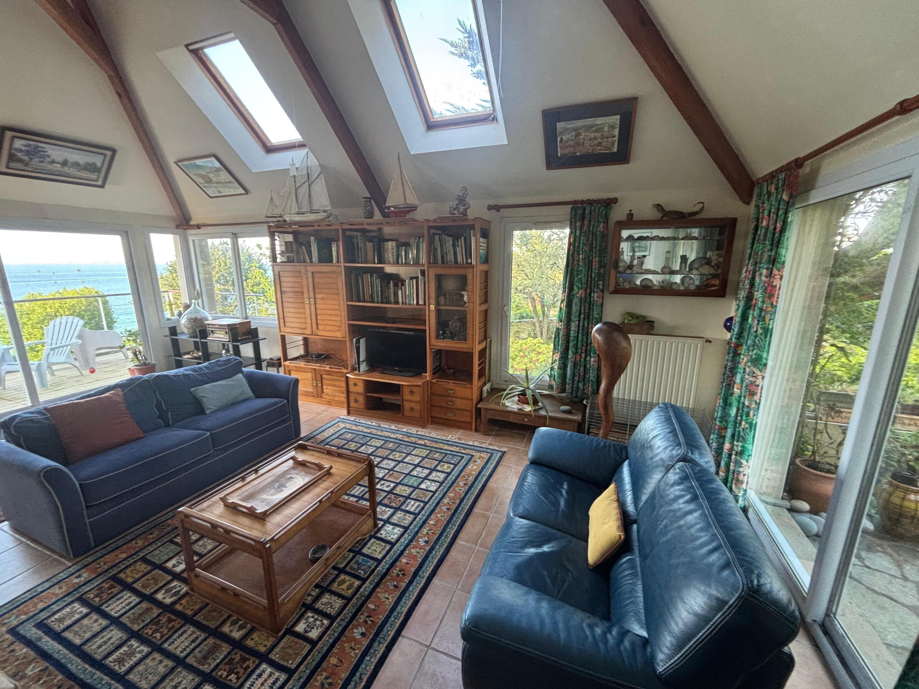 Ein Wohnzimmer mit einer Couch, einem Couchtisch, einem Bücherregal und Meerblick durch große Fenster.