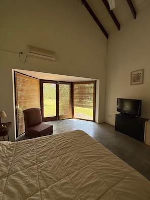 A bedroom with a bed, a chair, a television, and a view through a window.