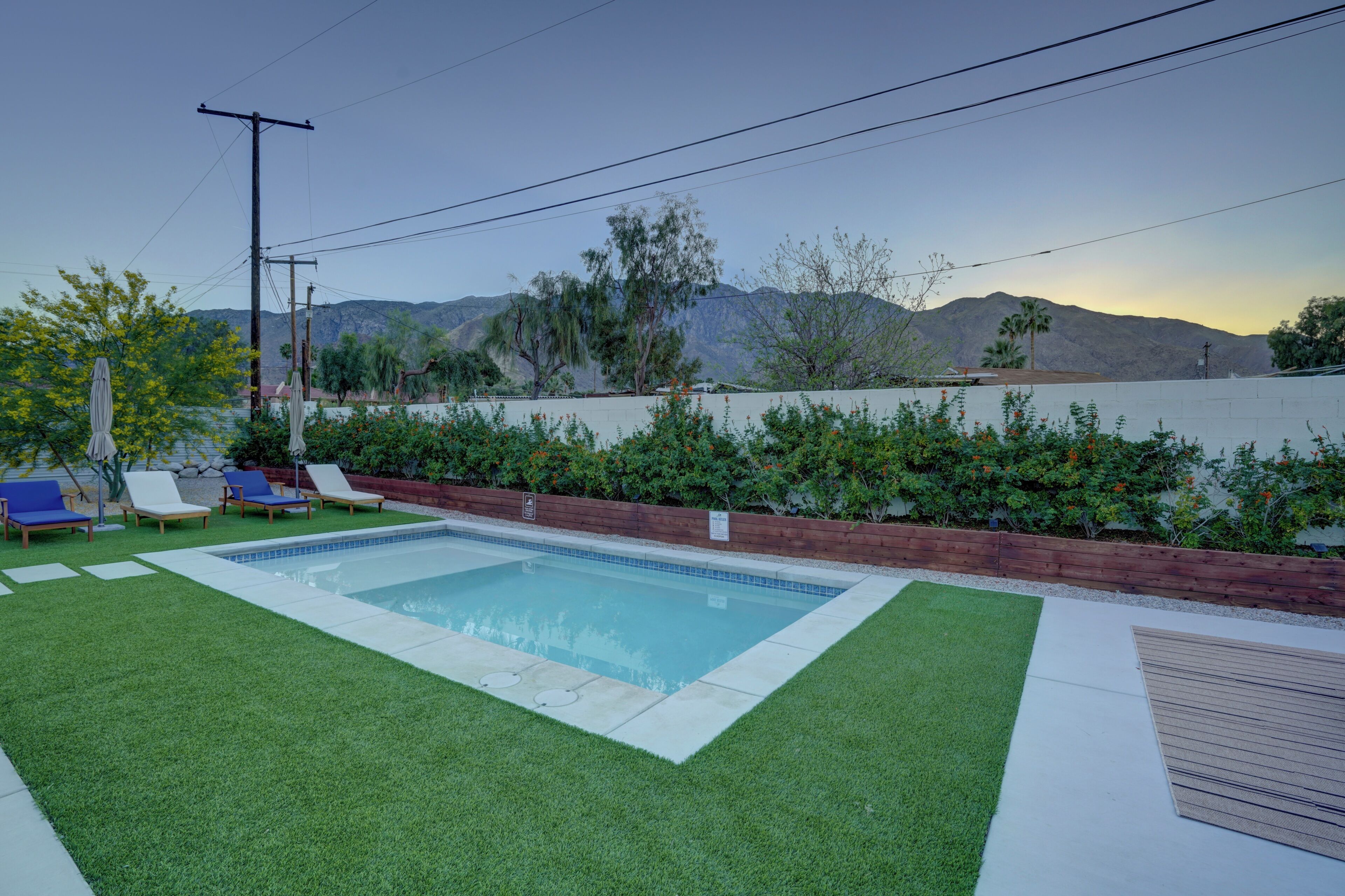 A swimming pool with artificial grass, lounge chairs, and a wooden deck.