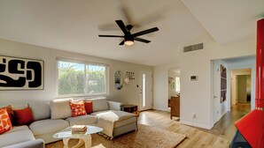 A modern living room with a sofa, coffee table, and a ceiling fan. - Vista Ashby: Stagecoach Oasis, Pool & Mtn Views (Palm Springs)