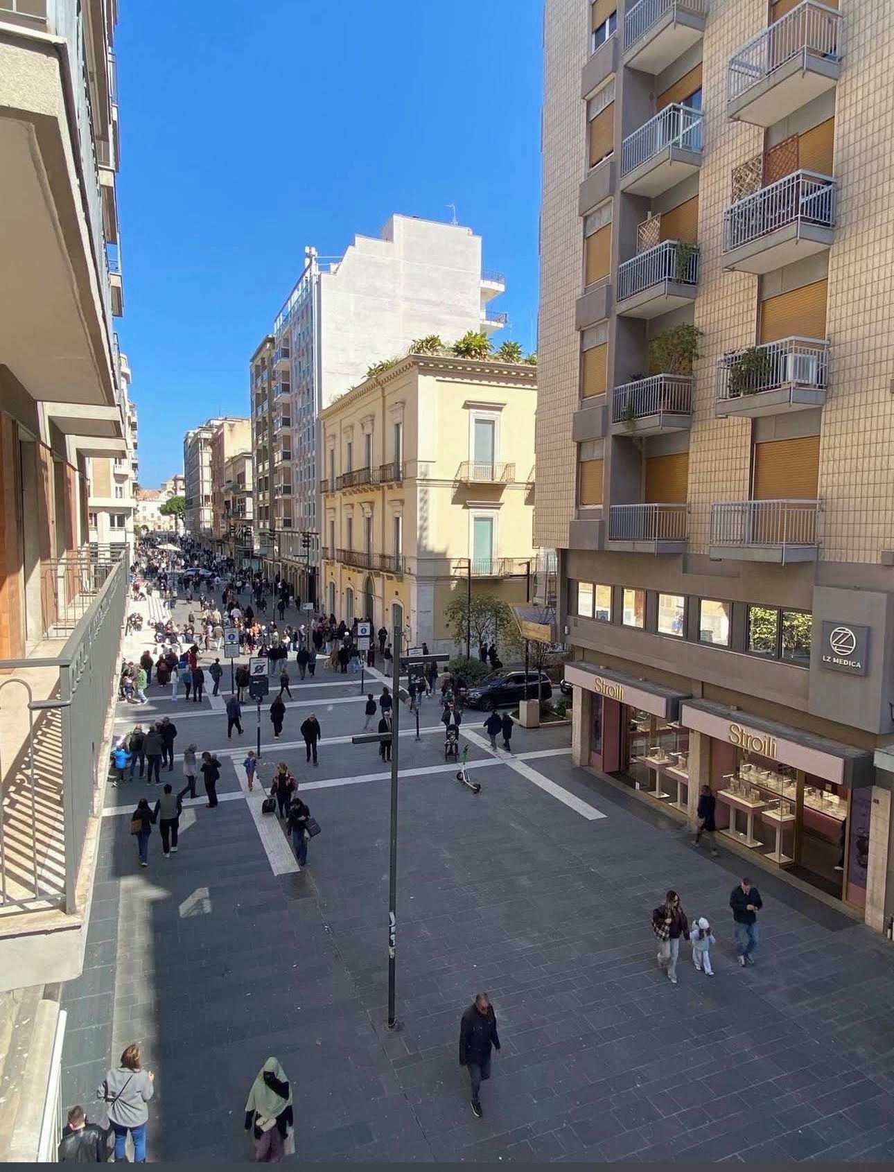 A pedestrian street lined with multi-story buildings, some with balconies, and storefronts.