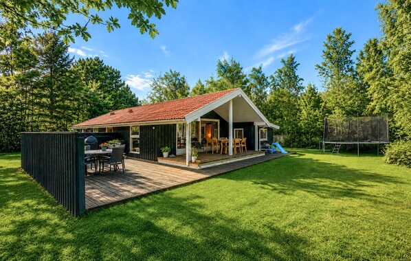 Une maison avec une terrasse, un espace barbecue et un trampoline.