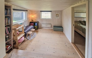 Une pièce avec un plancher en bois, une bibliothèque, un bureau avec une chaise, un lit et deux fenêtres.