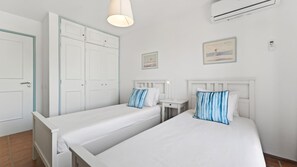 Une chambre avec deux lits, une armoire, une table de chevet, une lampe et un appareil de climatisation.