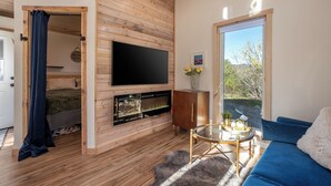 A room with a TV, wooden walls, a sofa, a small table, and a window with a view.