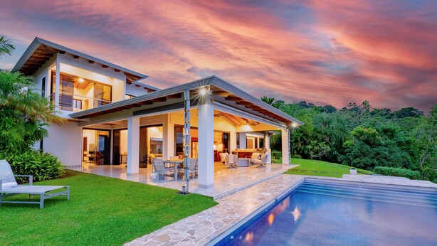 Une maison moderne à deux étages dotée d’un patio extérieur, d’une piscine et d’une végétation luxuriante.