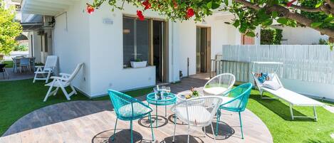 A patio with outdoor furniture, a small table, and a white building with a door and windows.