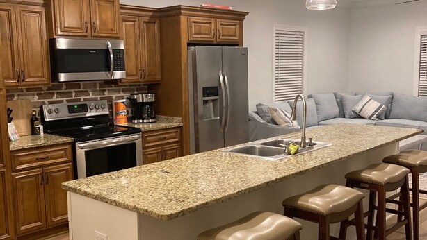 A modern kitchen with granite countertops, stainless steel appliances, wooden cabinets, and a central island with bar stools. - COMPLETELY REMODELED-- LESS THAN A BLOCK FROM BEACH--
HOT TUB-- NOON CHECK OUT!! (BAY ST LOUIS)