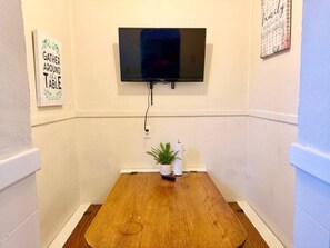 A room with a TV mounted on the wall, a wooden table with a small plant, and a sign that says 'Gather Around the Table'. - Large Group Stay Near Syracuse University & Dome (Syracuse)
