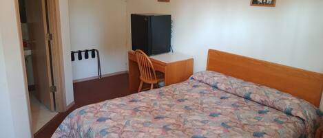 Ein Schlafzimmer mit einem Bett, einem Schreibtisch, einem Stuhl, einem Kleiderschrank und einem Bild an der Wand.